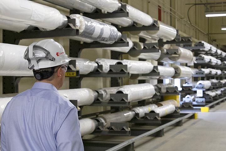 man wearing safety hat walking isle of warehouse rolls of membranes product